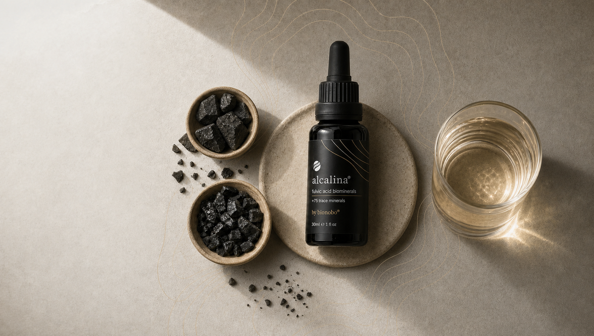 Alcalina fulvic-acid dropper bottle with mineral stones and a glass of clear golden water.