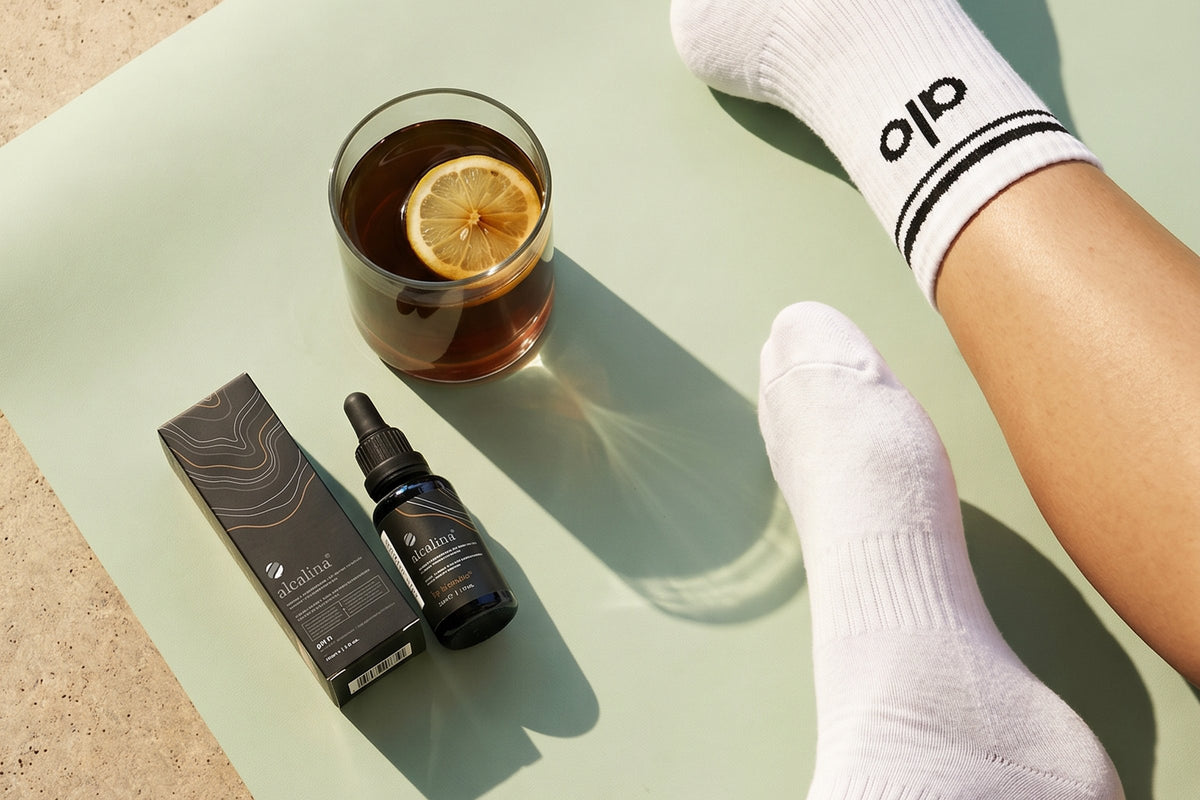 An alcalina dropper bottle and a glass of lemon tea beside a yoga mat