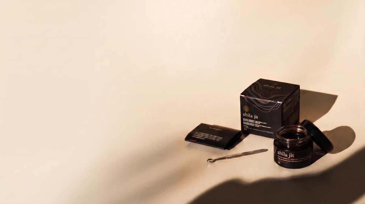 A Golden Shilajit resin jar beside its box, lid and dosing spoon on a cream surface.