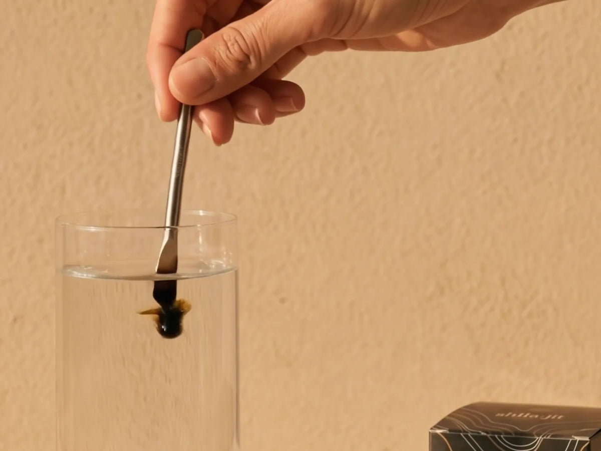 Golden Shilajit resin dissolving into clear water before a woman drinks the golden mineral ritual.